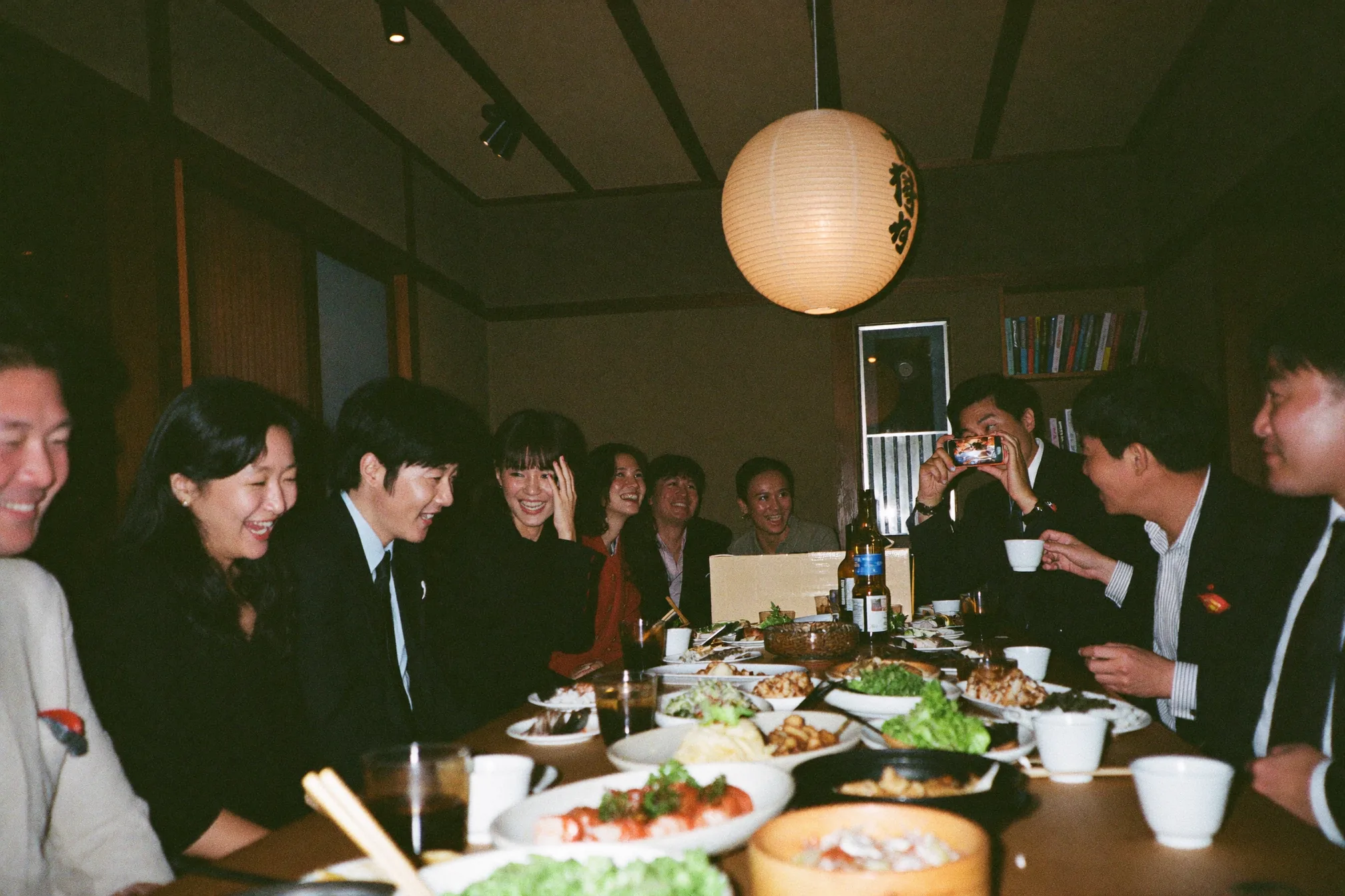 普通の会議室で開かれる社内クリスマスパーティー。ライトと卓上のキャンドルに照らされ、長机を囲んで談笑する同僚たち