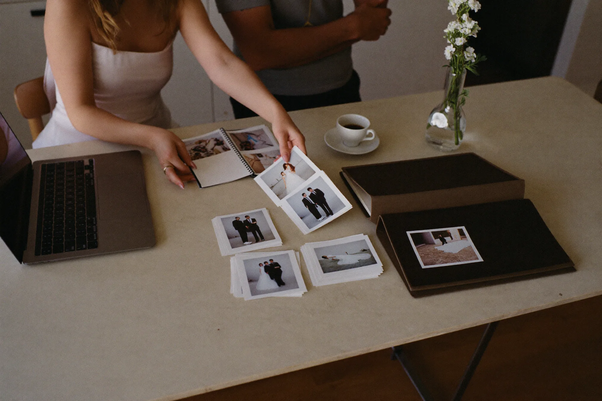 Una coppia al tavolo della cucina guarda le foto del matrimonio sul portatile, accanto un disco esterno e alcune stampe