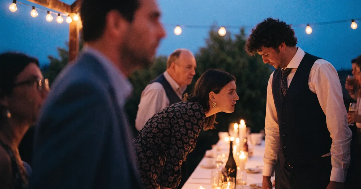 Guests mingling around a long candlelit table at an outdoor wedding reception at dusk.