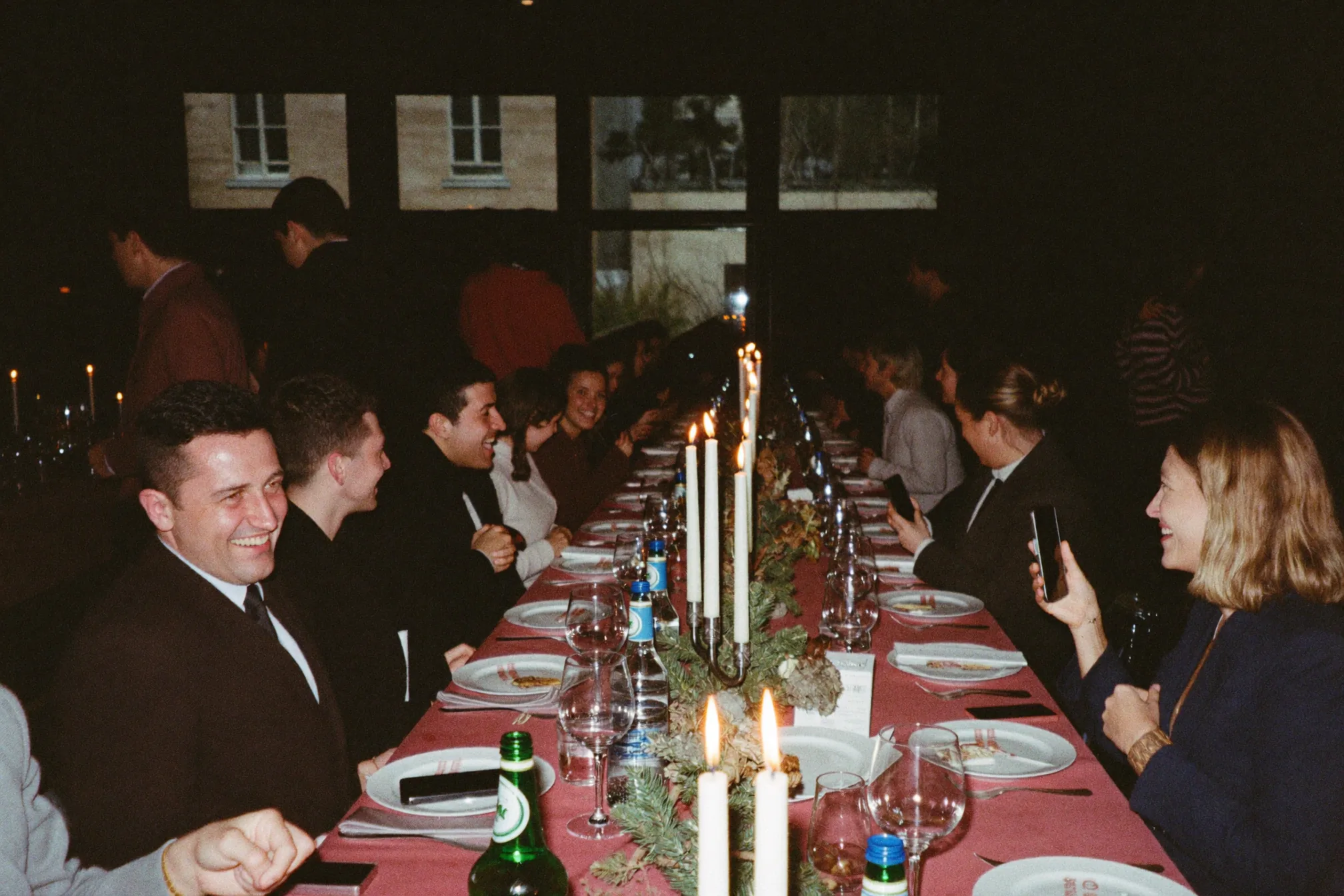 Weihnachtsfeier im nüchternen Besprechungsraum, mit Lichterketten und Teelichtern beleuchtet, Kolleginnen und Kollegen an einer langen Tafel