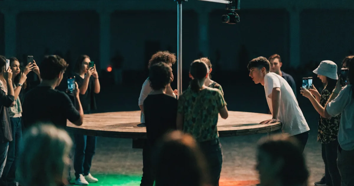 Party guests stepping onto a lit 360 photo booth platform while others photograph the moment on their phones.
