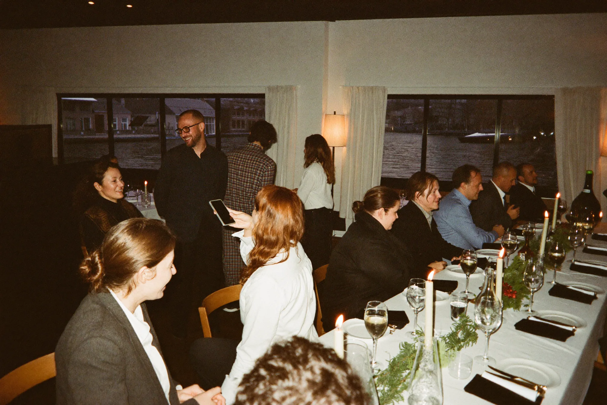 Kerstborrel op kantoor in een gewone vergaderzaal met lichtslingers en waxinelichtjes, collega's in gesprek rond een lange tafel