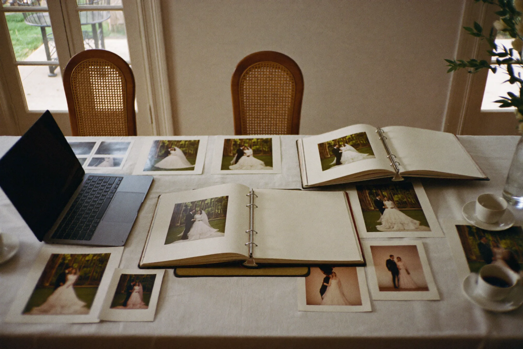 Couple à la table de la cuisine parcourant ses photos de mariage sur un ordinateur portable, un disque dur externe et quelques tirages à côté