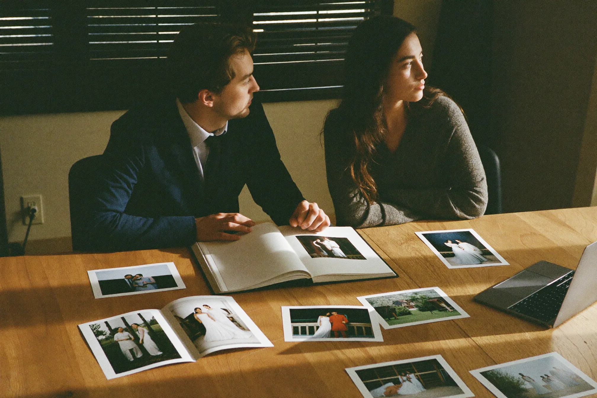 Pareja en la mesa de la cocina revisando las fotos de su boda en un portátil, con un disco externo y algunas copias impresas al lado