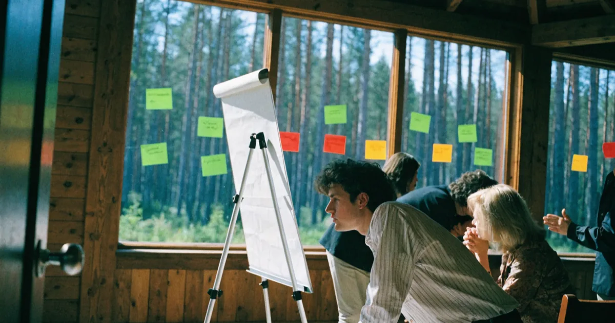 A team gathered in a lodge meeting room at a company retreat, flip chart mid-exercise and sticky notes stuck to the window behind them
