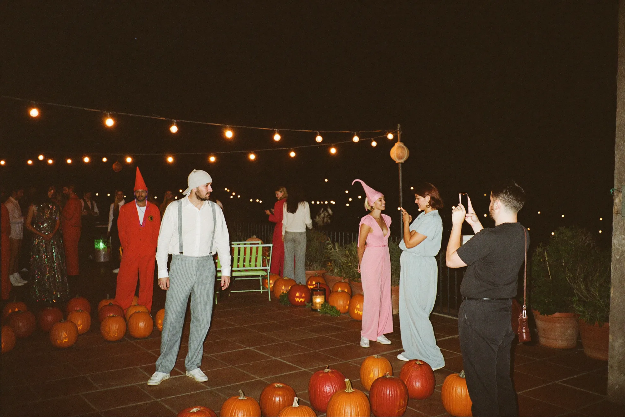 Invitados bailando en una fiesta nocturna mientras uno fotografía el momento con el móvil, con luz cálida suficiente para que se vean las caras