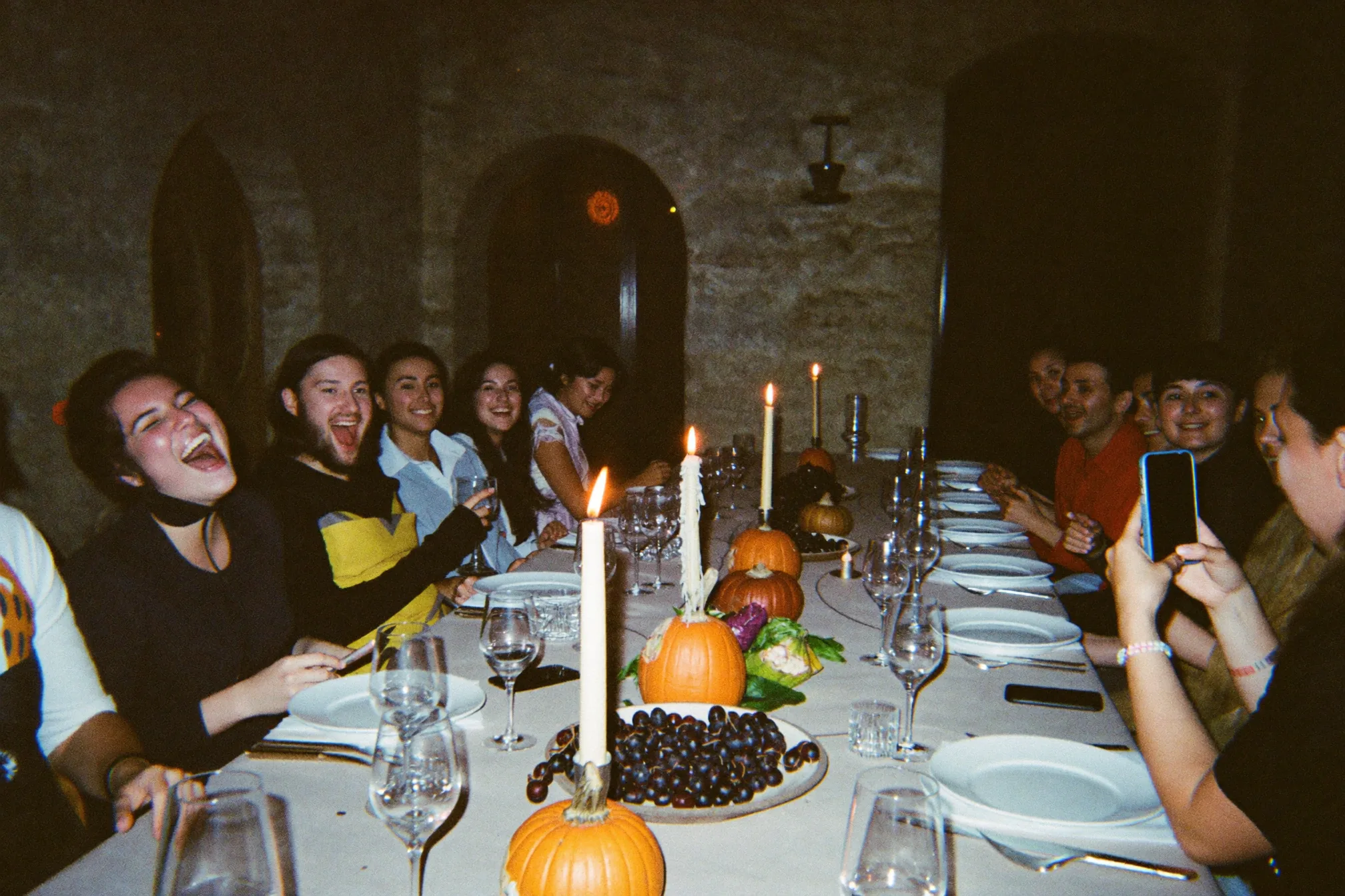 Ospiti che ballano a una festa serale mentre uno fotografa il momento con il telefono, con una luce calda che tiene i volti visibili