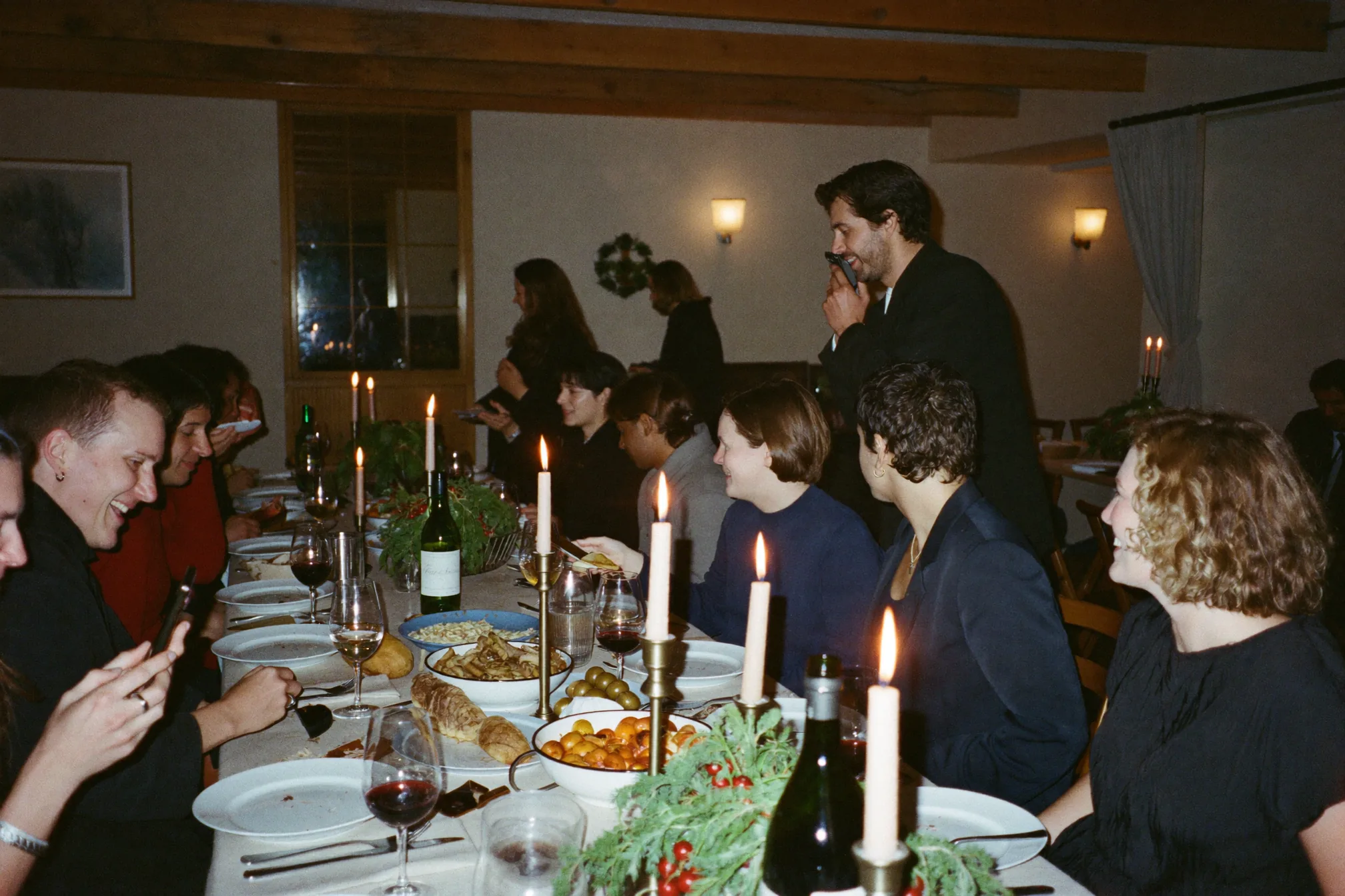 Festa di Natale in ufficio in una normale sala riunioni illuminata da lucine e candele, colleghi che parlano attorno a un lungo tavolo