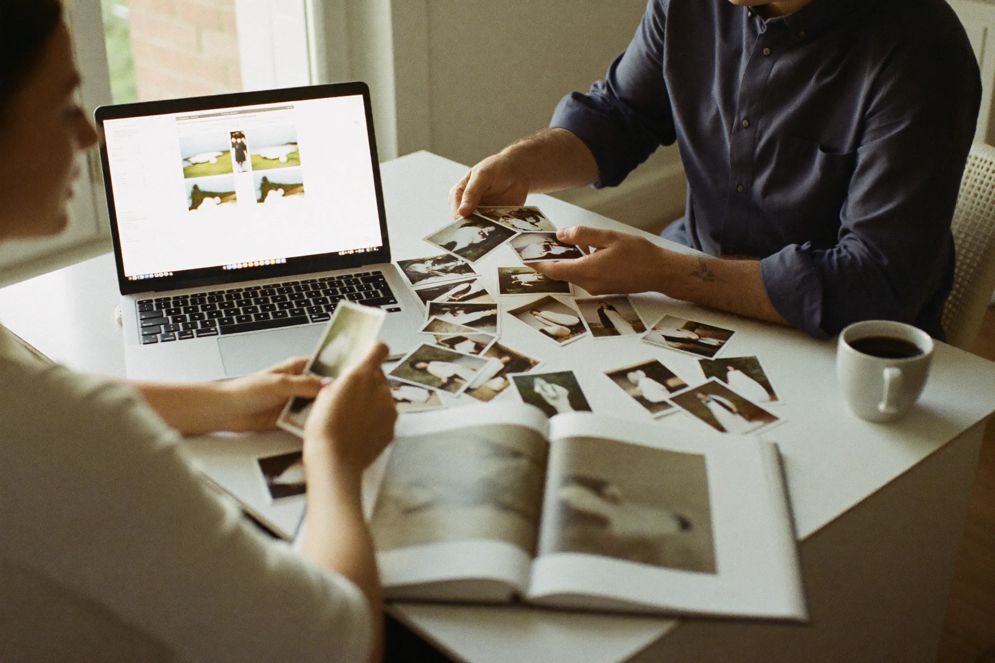 Paar am Küchentisch beim Durchsehen der Hochzeitsfotos am Laptop, daneben eine externe Festplatte und einige Abzüge